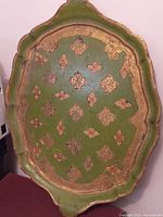Top side of antique Florentine tray showing green background with gold and red painted decorative patterns and scalloped edges.
