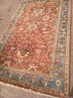 Full view of the wool rug with rust field and blue border showing the pattern and condition