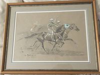 Framed hand tinted print showing two horses racing with jockeys. Visible artist signature on bottom left and numbered edition on bottom right.