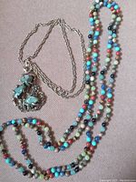 Full view of both necklaces showing the long multi-colored beaded necklace and the silver-tone chain with pendant
