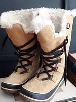 Side front view of the pair of beige SOREL winter boots showing black laces and white faux fur lining at the top.
