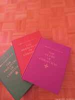 Top view of three hardcover Christmas books stacked: 'The Pageantry of Christmas' in green, 'The Merriment of Christmas' in red, and 'The Glory of Christmas' in magenta.