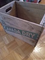 Wooden crate with Canada Dry The Champagne of Mixers logo on the side, displaying age and wear.