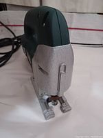Close-up of the Metabo electric jigsaw front end showing the blade clamp and part of the green handle with power cord attached.