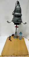 Photographic enlarger standing on wooden base with water bottle for scale, showing front and base.
