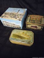 Three vintage tins arranged together on a black cloth, showing each tin's top print: Trafalgar Square scene on large square tin, Public Benefit Boat Company ad on square tin, ocean liner ship on smaller rectangular tin.