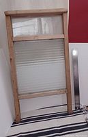 Vintage washboard standing upright next to a metal ruler for scale, placed against a white and red background.