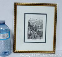 Front view of framed vintage signed etching with water bottle for size perspective. Etching shows mountain, church, forest scene.