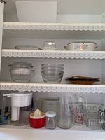 Multiple shelves showing Pyrex mixing bowls, baking dish with floral pattern, pitcher, hand juicer, butter dish, measuring cups and glasses