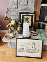 Overview of collection showing brass elephant, brass vase, lighthouse lamp, framed print and wall clock on stone and wood surface.