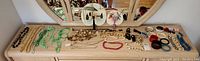 Full view of the costume jewelry including necklaces, bracelets and decorative hand fans on a white surface in front of a mirror.