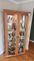 Full front view of the wooden display cabinet filled with various porcelain figurines showing structure and contents.