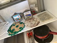 Photo showing two decorative trivets, two framed decorative items, and a square marble trivet on shelf. Also partially showing fondue pot below.