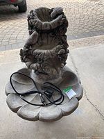Full view of the two-tier garden fountain with leaf and bird detailing, showing the included electric pump and power cord lying in the base bowl.