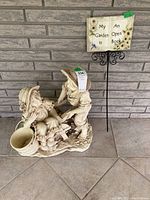 Overall view of garden plaque and figurine showing both items together against a brick wall.