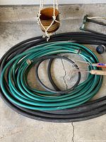 Coiled green and black hoses along with hanging terracotta pots and hand gardening tools placed on the floor.