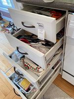 Top drawer of kitchen cabinets with assorted kitchen utensils such as spoons, scoops, openers, and dish towels inside