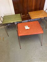 Three MCM stacking stools in green, orange, and tan colors, placed on garage floor showing front and side views.