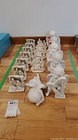 Entire lot of unpainted white figurines arranged on the floor. Includes several nativity sets and angels.
