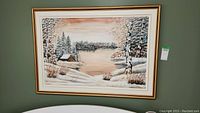 Full framed winter landscape painting depicting a cabin by a frozen lake, snow-covered trees, and a warm sky.