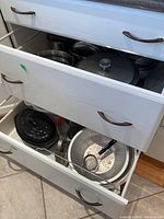 Drawers opened showing various kitchen items including pots, pans, colander, masher and funnel.