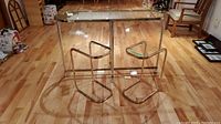 Two brass framed side tables with glass tops standing on a hardwood floor.
