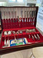 Full view of Oneida Tudor Plate silver plate flatware set displayed in velvet red-lined wooden canteen, including knives, forks, spoons, and serving utensils.