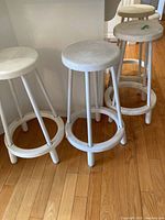 Four white bar stools arranged together, showing the round seats and base design
