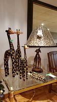 Photo of table lamp with giraffe-shaped wooden stem, leopard print lampshade, and four wooden giraffe figurines on glass table.