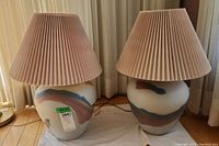 Two identical table lamps side by side with ceramic bases painted with abstract multi-color brush strokes and pleated pink fabric shades.