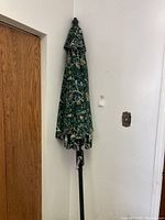 Full closed outdoor umbrella hanging on wall next to wooden door, showing entire height and crank handle on pole.