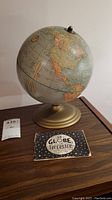 Photo of the vintage terrestrial globe showing North and Central America, mounted on a gold-colored metal stand, with the original instruction booklet in front.