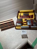 Full view of the closed yellow and brown zippered travel case with metal toiletry items and the wooden crate next to it.