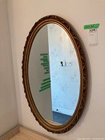 Full view of oval wall mirror with ornate gold frame on wall, showing size note of 20x32