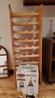 Wooden wine rack with rectangular frame and multiple curved shelves for holding wine bottles. Bravetti Wine Chiller box placed in front of the rack.