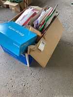 Photo of two cardboard boxes containing assorted wrapping paper sheets, many Christmas-themed, and gift bags in different colors including red, green, and white.