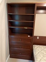 Front view of the full wood cabinet with shelves and drawers next to a bed.