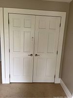 Pair of white painted interior closet doors installed in a frame, each door has six panels with rectangular recessed designs.