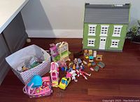 Overview of the green dollhouse, fabric bin, and assorted toys spread around, showing condition and contents.
