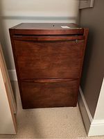 Front view of wood two drawer file cabinet showing locked top drawer and overall condition.