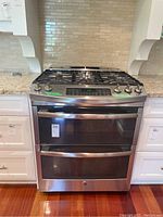 Front view of stainless steel GE Profile gas stove embedded between white cabinetry showcasing the five burners and dual oven setup.