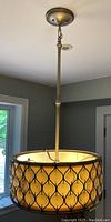 Full view of hanging light fixture with metal rod, ceiling mount, and drum shade with decorative metal pattern and amber glass panels.