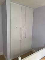Front view of the white three-door IKEA Forsand cabinet closed against a light purple wall.