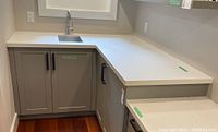 View of L-shaped counter height lower cabinet set with gray doors and black handles, white countertop, excluding sink and faucet.
