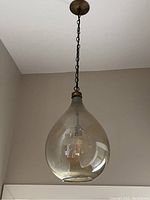 Photo showing teardrop-shaped clear glass shade with inner bulb socket and dark metal chain mount attached to ceiling.