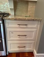 Front view of the white lower kitchen cabinet with three drawers closed, showing metal pull handles and smooth white finish