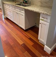 Three-section run of white lower cabinets under granite countertop with integrated sink