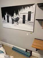 Large black and white abstract painting on stretched canvas hanging on wall with partial view of wood shelf below.