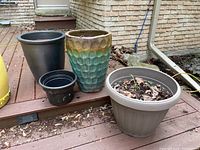 Four planter pots displayed outside on a wooden deck next to a house wall. Two glazed terra cotta and two plastic pots visible, with some damage on the blue glazed terra cotta pot.