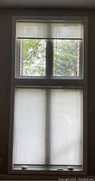 View of two white light filtering solar powered blinds installed on window, showing top and bottom blinds in natural light.